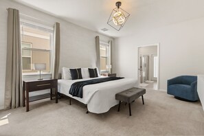Une chambre d’hôtel avec un grand lit, des tables de chevet, un banc, un bureau, une chaise et un luminaire moderne.