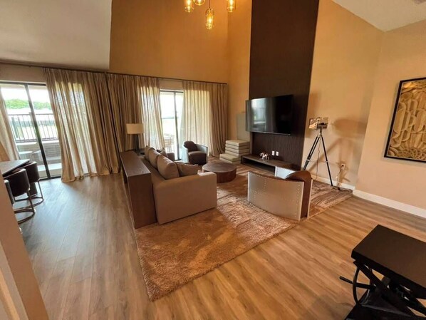 Een moderne woonkamer met een zithoek, een flatscreen televisie en een eettafel.