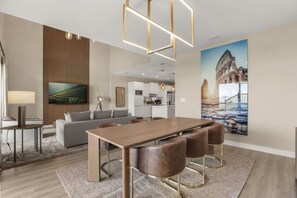A modern living room with a dining area, a kitchen in the background, and a large painting of a historical building. - Brand New! 3 Bd/3.5 Ba/ Magic Village by Pininfarina - 5591 PW (Kissimmee)