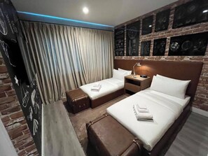 Een hotelkamer met een accentmuur van baksteen, twee bedden, een nachtkastje en een gordijn.