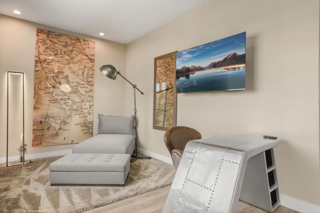 A bedroom with a bed, a desk, a chair, a map on the wall, and a painting.