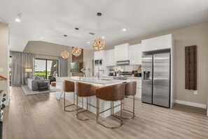 A modern kitchen with a central island, stainless steel appliances, and bar stools. - Brand New! 3 Bd/3.5 Ba/ Magic Village by Pininfarina - 5591 PW (Kissimmee)