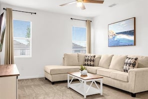Ein Wohnzimmer mit einem beigefarbenen Ecksofa, einem Couchtisch und einem Deckenventilator.