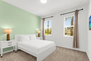 Een slaapkamer met een bed, twee nachtkastjes, een raam met gordijnen en een lichtgroene muur.