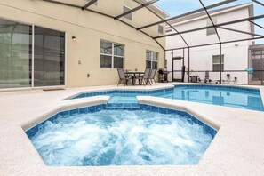 Une piscine avec un jacuzzi, entourée d’un patio couvert comprenant une table et des chaises.