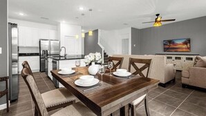 A modern kitchen with stainless steel appliances, a dining area with a wooden table and chairs, and a living room with a sofa and a painting on the wall. - 8 BD/ 5 BA/ Bella Vida (4489 MD) (Kissimmee)