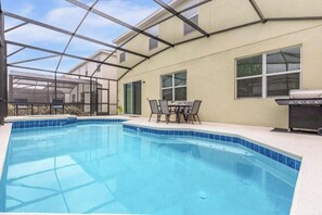 Ein Schwimmbad mit Glasüberdachung, ein Terrassentisch und ein Grillplatz.