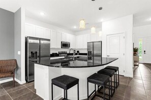 A modern kitchen with white cabinetry, stainless steel appliances, a central island with bar stools, and pendant lighting. - 8 BD / 5 BA /  Bella Vida 4489 MD (Kissimmee)