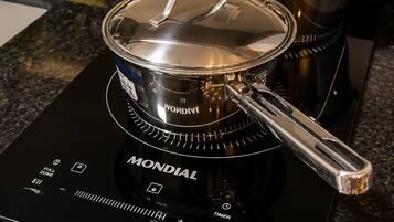 A kitchen with a black induction cooktop, two stainless steel pots, a yellow sponge, and a black soap dispenser.