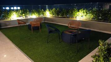 A rooftop terrace with artificial grass, wicker chairs, and potted plants.