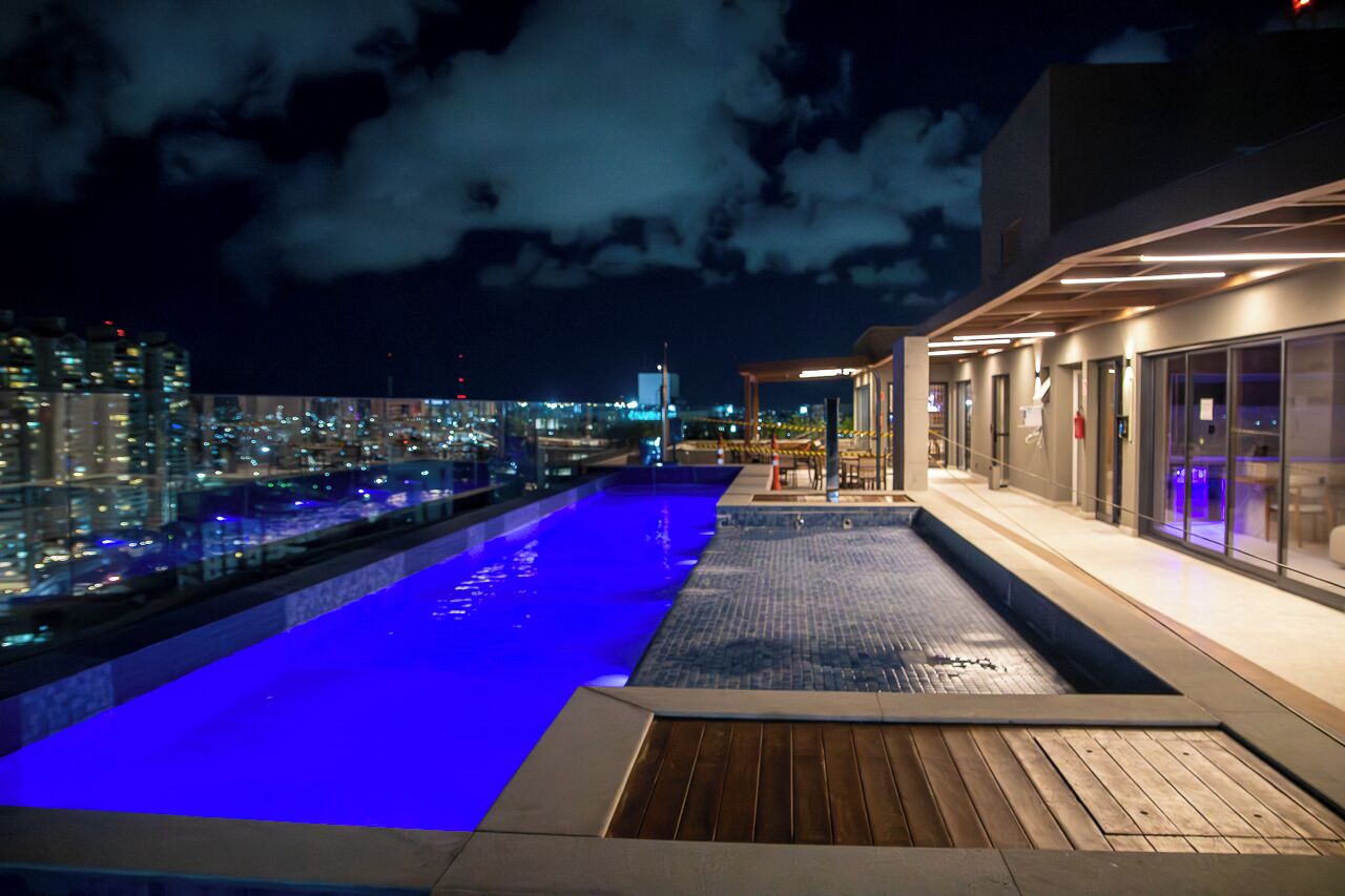 Une piscine sur le toit offrant une vue sur la ville, un espace salon couvert et une façade de bâtiment moderne.