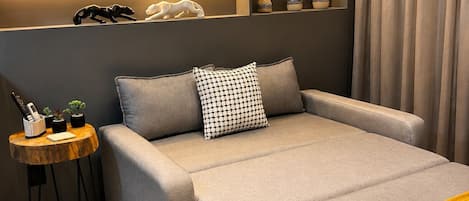 Un dormitorio moderno con sofá cama, una mesita auxiliar, una manta amarilla y un estante de pared con objetos decorativos.