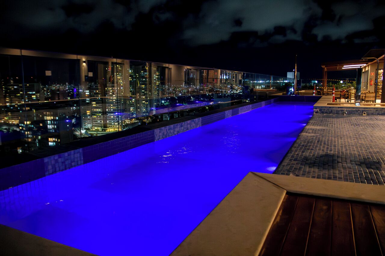 A rooftop pool with a city view, a covered seating area, and a glass barrier.