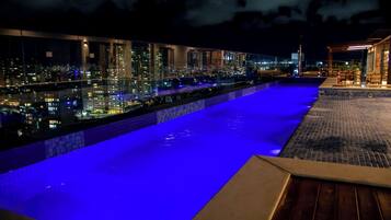 A rooftop pool with a city view, a covered seating area, and a glass barrier.
