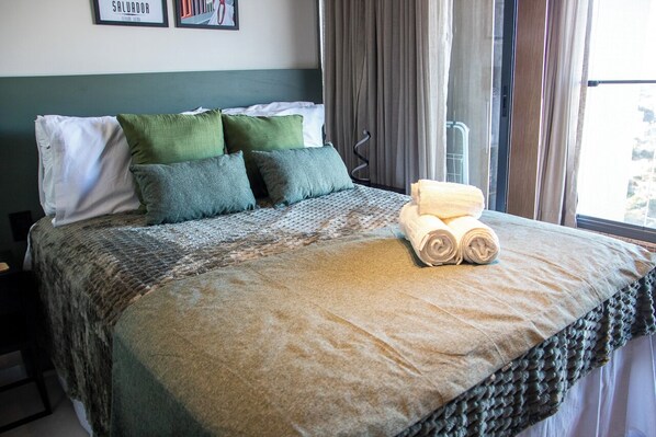 A neatly made bed with a rolled towel, green and white pillows, and a patterned bedspread.