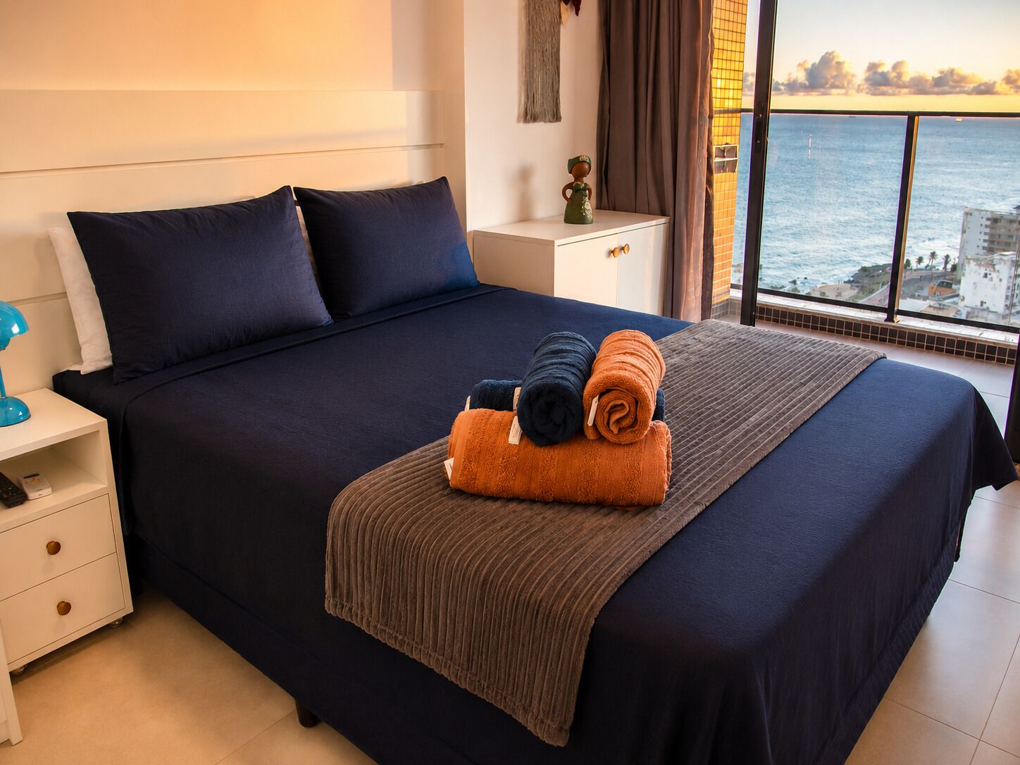 Una habitación de hotel con una cama grande, una mesita de noche, un aparador y vista al océano.