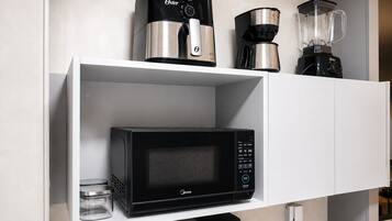 A kitchen shelf with a black Oster coffee maker, a black Oster coffee pot, a black Oster blender, and a black Oster microwave.