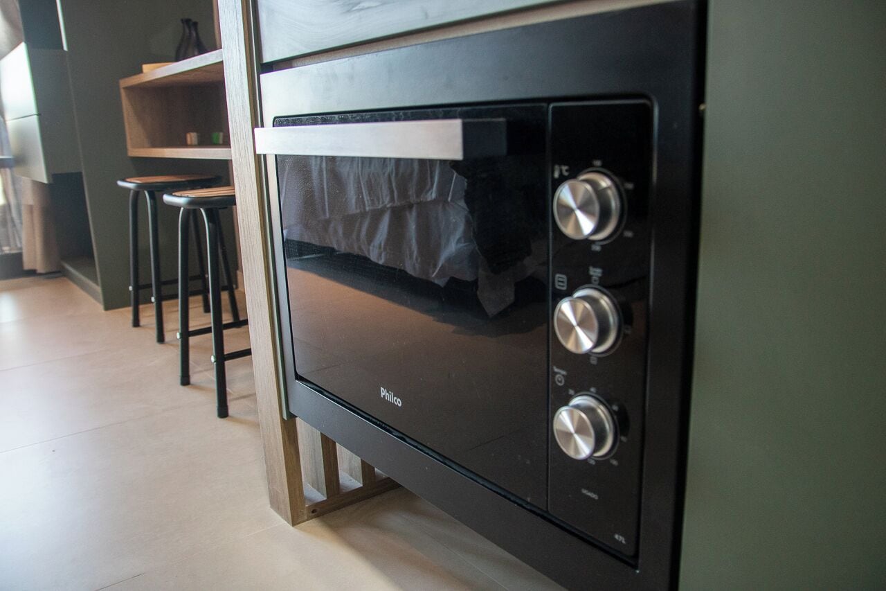 Una cocina con horno empotrado, repisa de madera y dos taburetes negros.