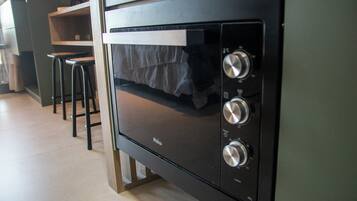 Una cocina con horno empotrado, repisa de madera y dos taburetes negros.