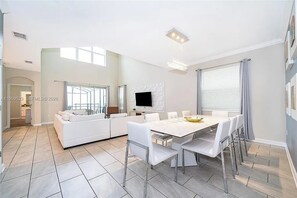 A modern kitchen with a dining area, white furniture, and a flat-screen TV. - 5 BD/ 5 BA/ Storey Lake (4352 QS) (Kissimmee)