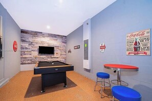 A billiards table with a pool cue, a television mounted on a stone-textured wall, and a Coca-Cola poster. - 5 BD/ 5 BA/ Storey Lake (4352 QS) (Kissimmee)