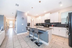 A modern kitchen with white cabinets, a central island with bar stools, and a black refrigerator. - 5 BD/ 5 BA/ Storey Lake (4352 QS) (Kissimmee)