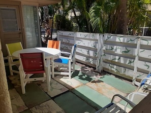 An outdoor patio area with a table and chairs, a white fence, and palm trees in the background. - Turtle Crawl Villa 81 (Longboat Key)