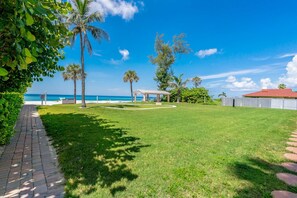Un espace verdoyant agrémenté d’un kiosque, de palmiers et offrant une vue sur la plage.