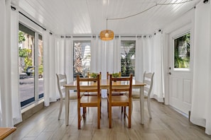 Un coin repas avec une table et des chaises en bois, des rideaux blancs et un luminaire suspendu.