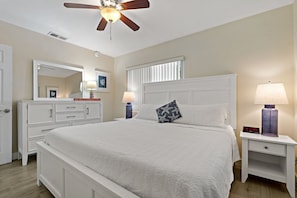 A bedroom with a bed, a nightstand, a dresser, a ceiling fan, and a window with blinds. - Turtle Crawl Villa 81 (Longboat Key)