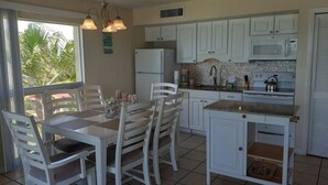 A kitchen with white cabinets, a dining table with chairs, and a small island. - Beach view unit  504 (Longboat Key)
