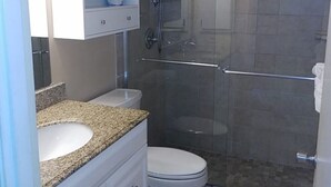 A bathroom with a glass-enclosed shower, a white toilet, and a granite countertop sink. - Beach view unit  504 (Longboat Key)