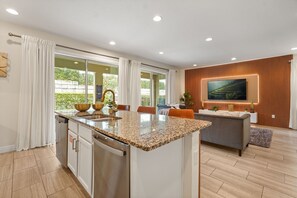 A modern kitchen with a granite countertop, a built-in dishwasher, and a dining area with a sofa and a TV mounted on the wall. - 5 BD/ 5 BA/ Encore Resort at Reunion (280 PC) (Kissimmee)