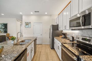 A modern kitchen with granite countertops, stainless steel appliances, and white cabinetry. - 5 BD/ 5 BA/ Encore Resort at Reunion (280 PC) (Kissimmee)