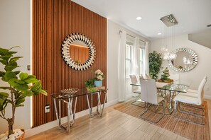 Ein moderner Essbereich mit einem Glastisch, weißen Stühlen und einer Wand mit Holzverkleidung.