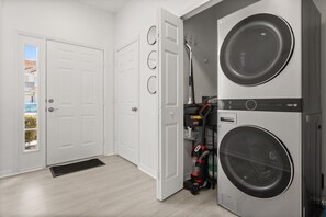 A laundry room with two stacked washing machines, a vacuum cleaner, and a door leading to a balcony. - 3 BD/ 2.5 BA/ Fiesta Key (1286 SB) (Kissimmee)