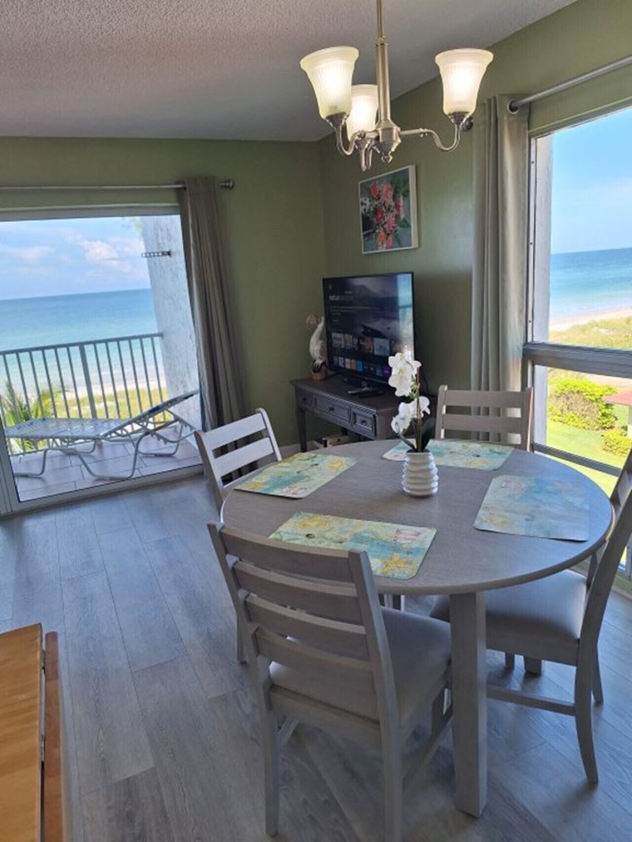 A dining area with a view of the ocean, a television on a stand, and a chandelier.