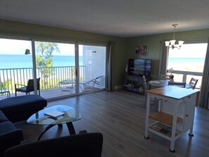 A living room with a glass table, a sofa, a TV, and a balcony with a view of the sea. - Beach view unit  404 (Longboat Key)