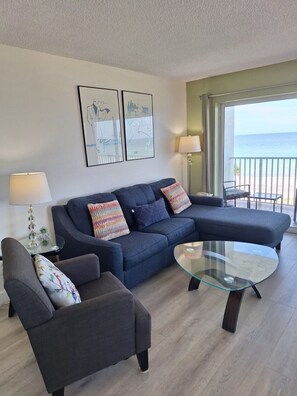A living room with a sofa, armchair, and glass coffee table. There are two wall-mounted lamps and a framed artwork above the sofa. - Beach view unit  404 (Longboat Key)