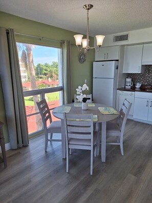 A dining area with a table and chairs, a refrigerator, and a window with curtains. - Beach view unit  404 (Longboat Key)