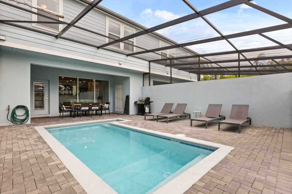A swimming pool with lounge chairs, a barbecue grill, and a covered patio area.