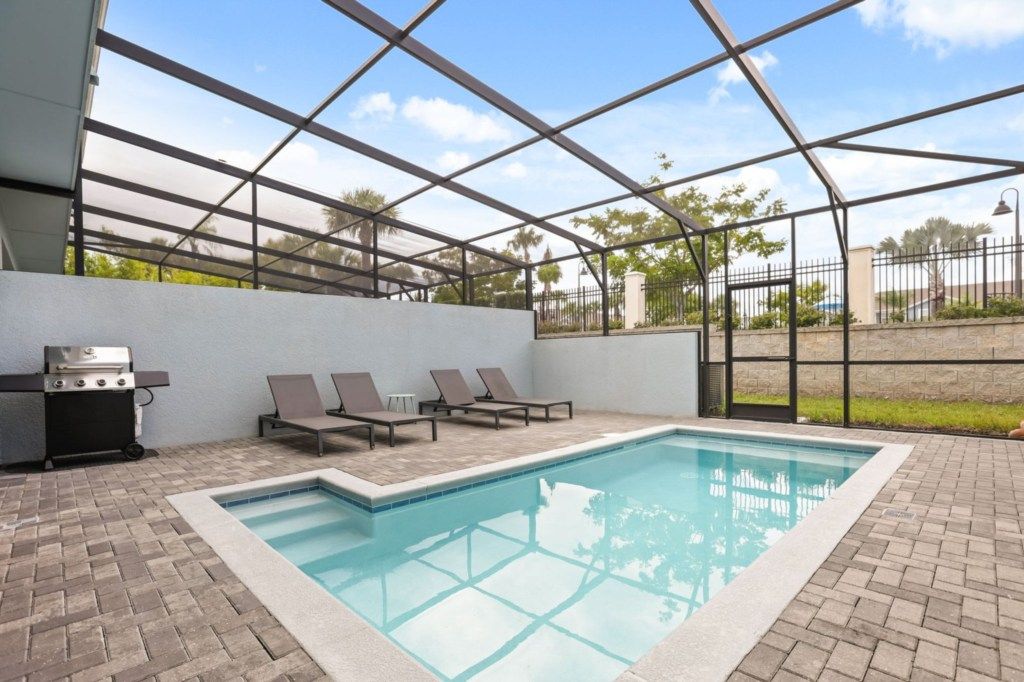 Un área de piscina con parrilla, sillas de descanso y un porche cubierto.