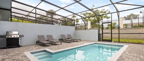 Un área de piscina con parrilla, sillas de descanso y un porche cubierto.
