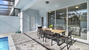 Eine Außenpatio mit Pool, einem Esstisch mit Stühlen und einer Glastür zum Deck.