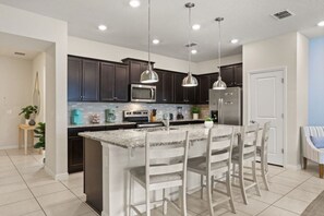 A modern kitchen with dark cabinets, stainless steel appliances, and a central island with bar stools. - Windsor Island Oasis! Sleeps 12 - 131 JW (Davenport)