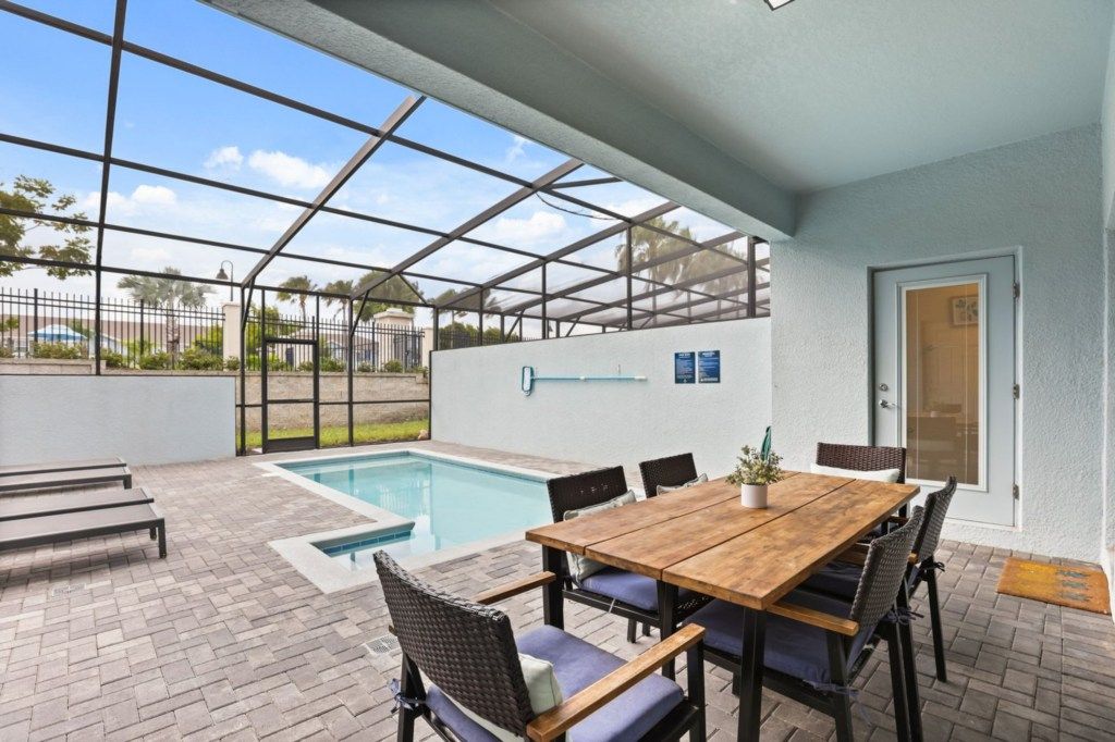 Un espacio al aire libre cubierto con piscina, una mesa de madera con sillas y una puerta.