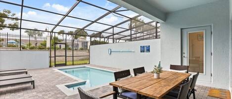 Un espacio al aire libre cubierto con piscina, una mesa de madera con sillas y una puerta.
