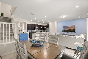A modern kitchen with dark cabinets, a dining area with a wooden table and white chairs, and a living area with a sofa and a painting on the wall. - Windsor Island Oasis! Sleeps 12 - 131 JW (Davenport)