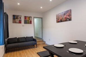 Ein Wohnzimmer mit einer Couch, einem Esstisch für zwei Personen und einer Treppe zu einer oberen Etage.
