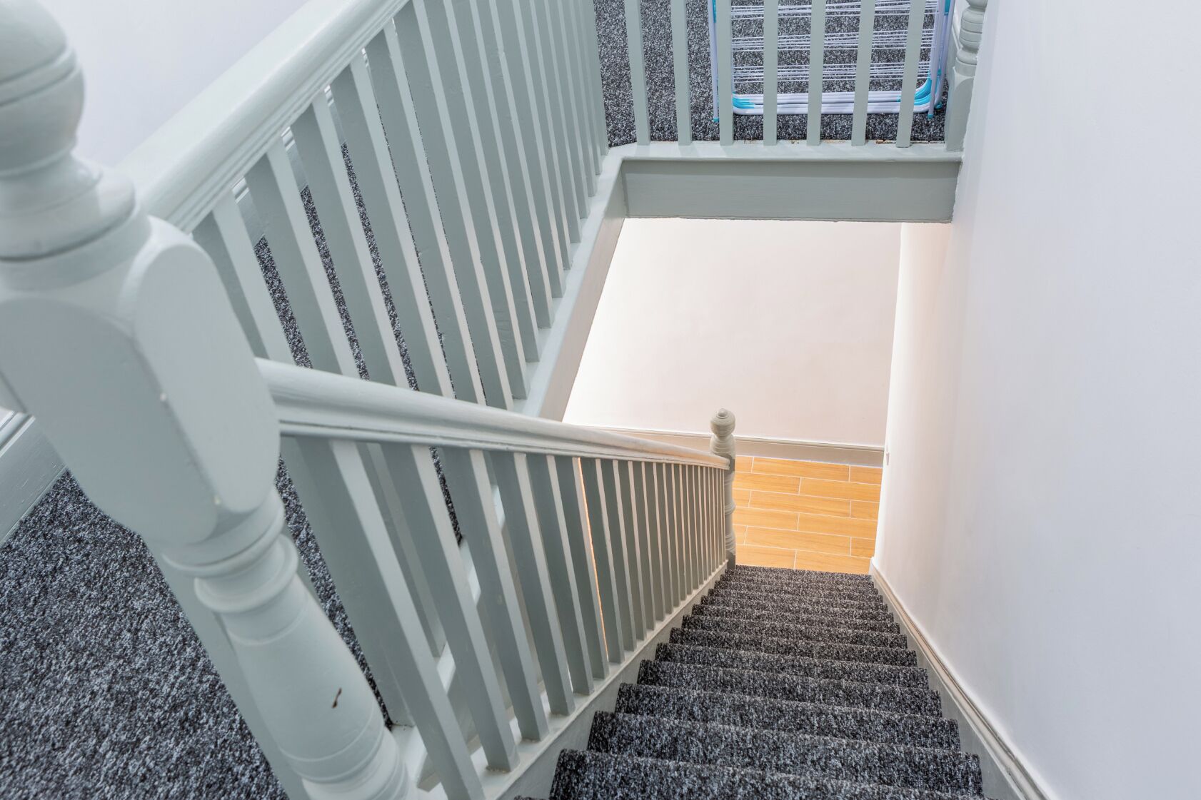 A staircase with white railings and a carpeted floor leading to a room with a brick wall.